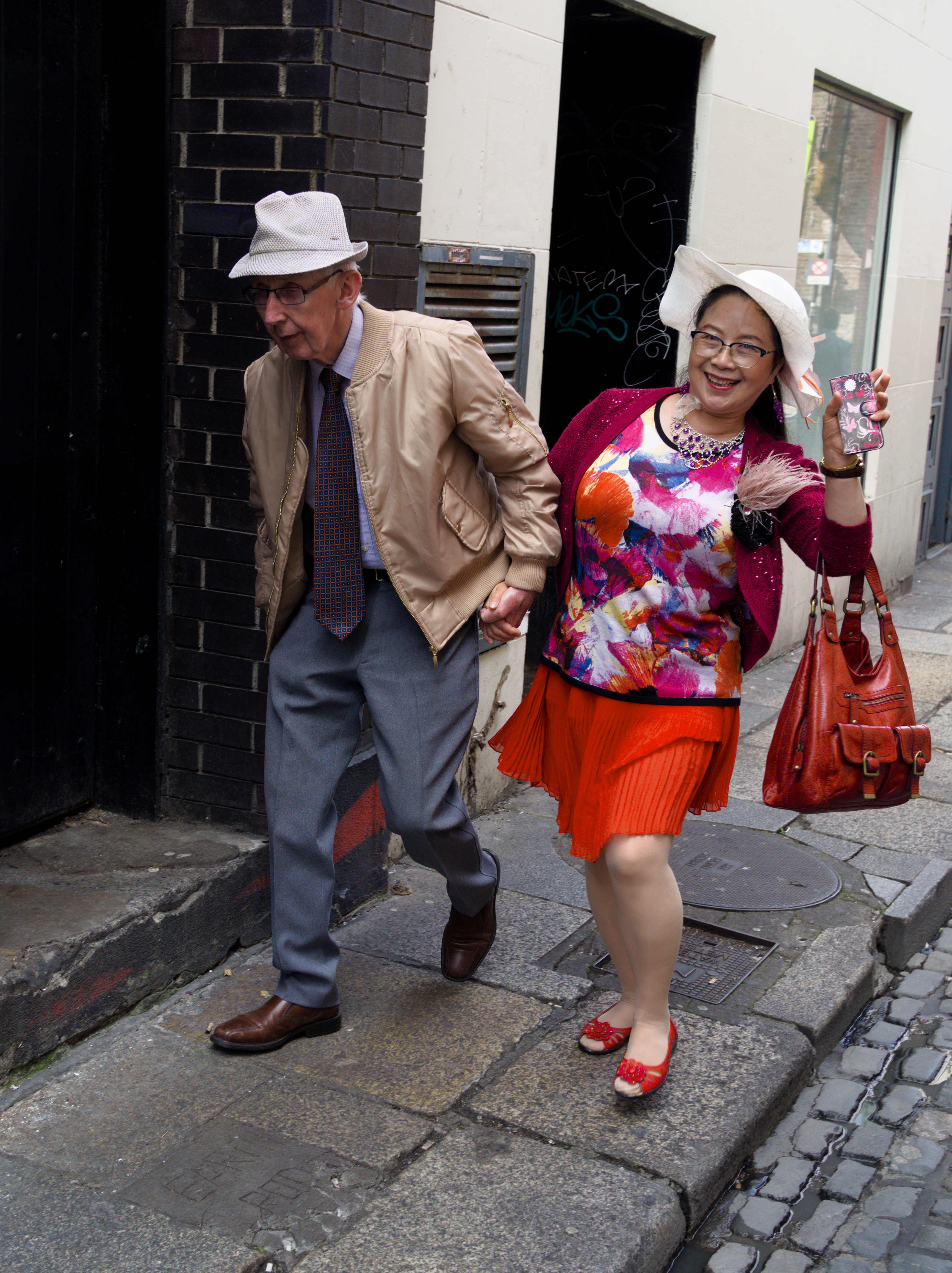 Older couple walking hand in hand, with colourful clothing.