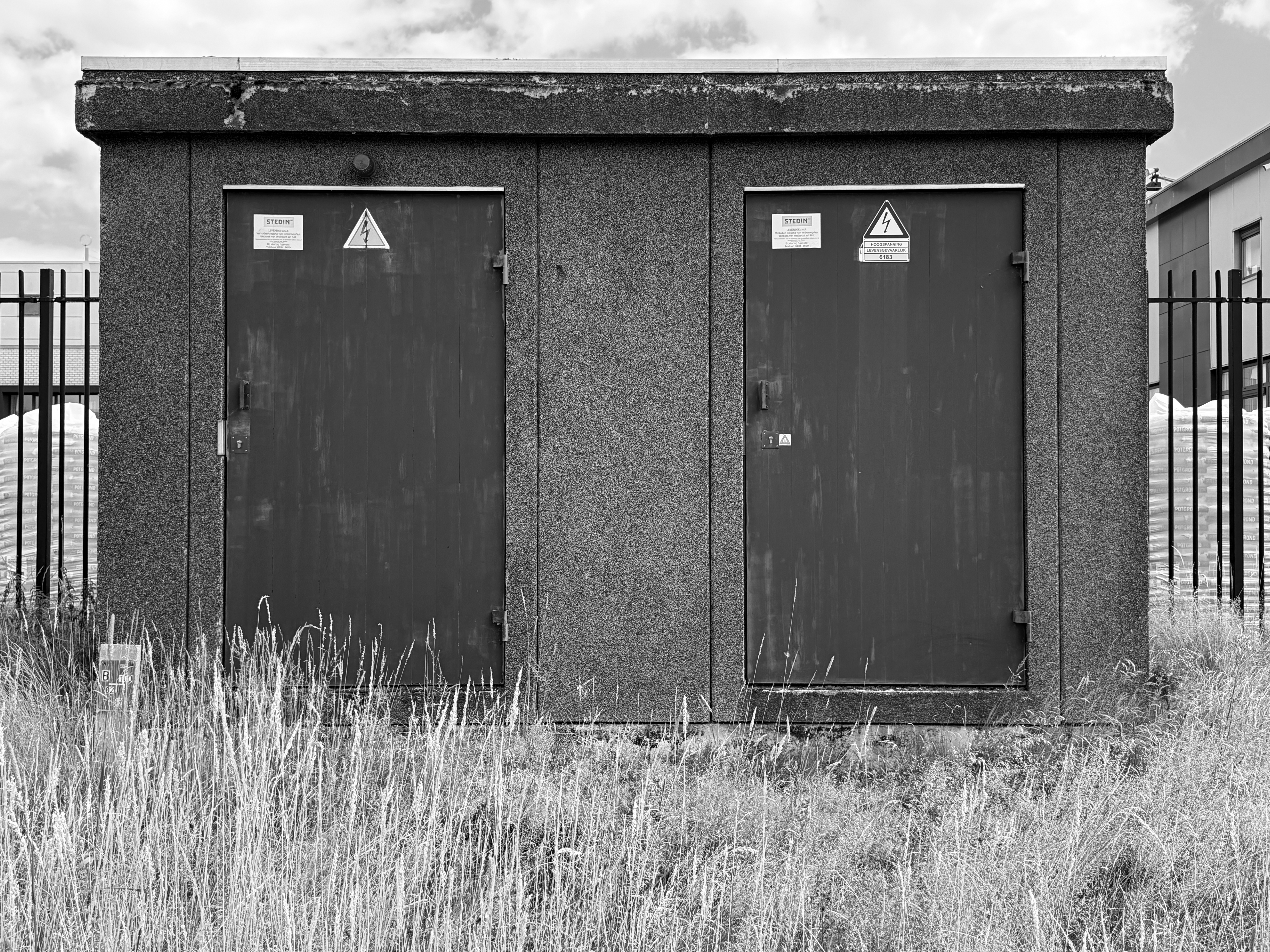 Utility building with technical doors and tall grass in black and white.